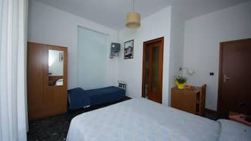 A bedroom with a bed, a wooden wardrobe, a small desk with a chair, a television, and a door.