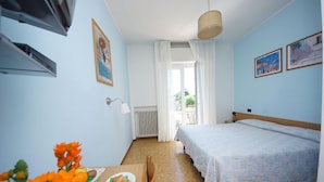 Een kamer met een bed, een tafel met een bord en bloemen, een radiator en een raam met gordijnen.