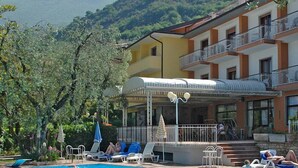 Een zwembad met ligbedden en parasols, omringd door een gebouw met balkons en uitzicht op een bergachtig landschap.