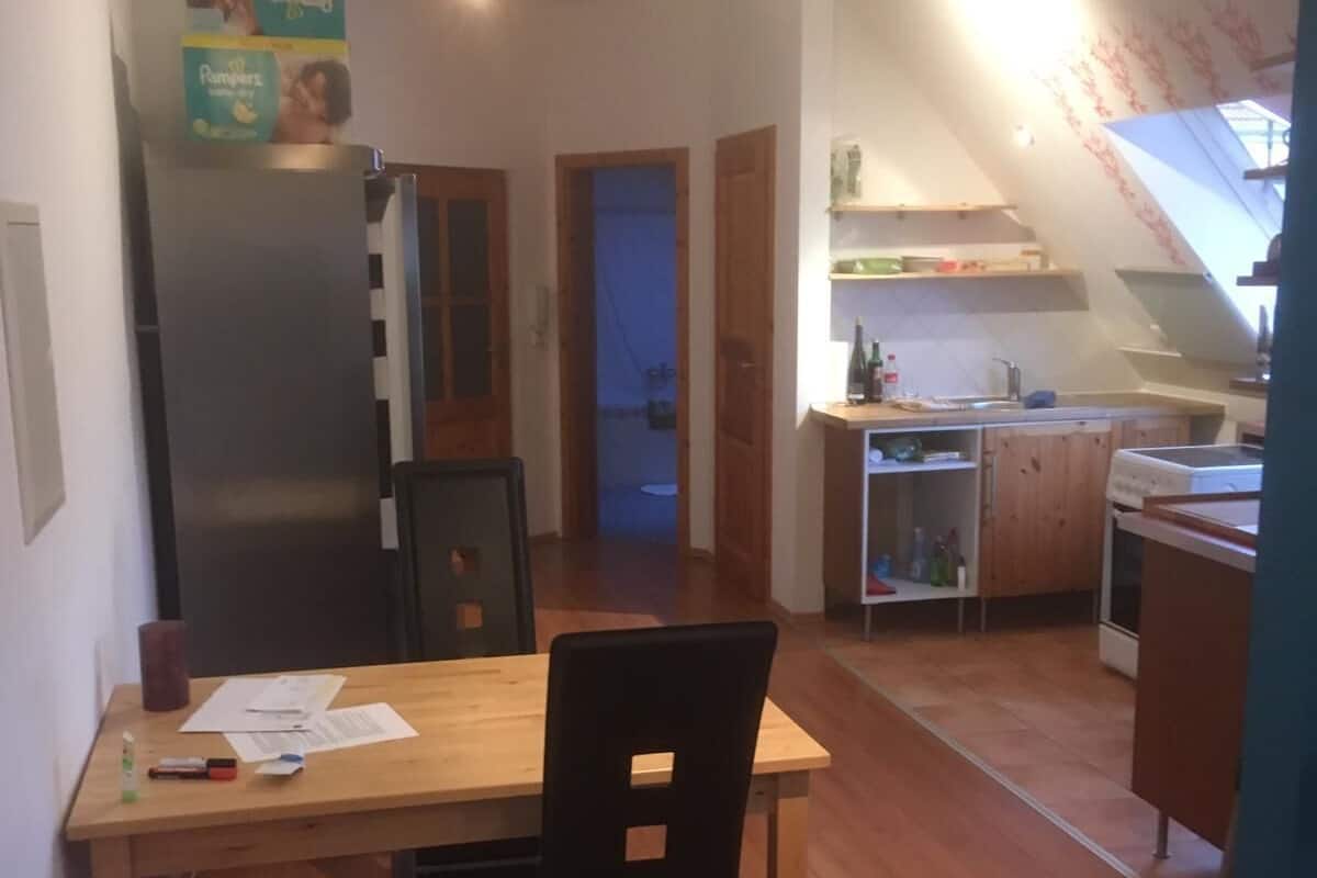Una cocina compacta con refrigerador, armarios de madera y un pequeño comedor con mesa y sillas.