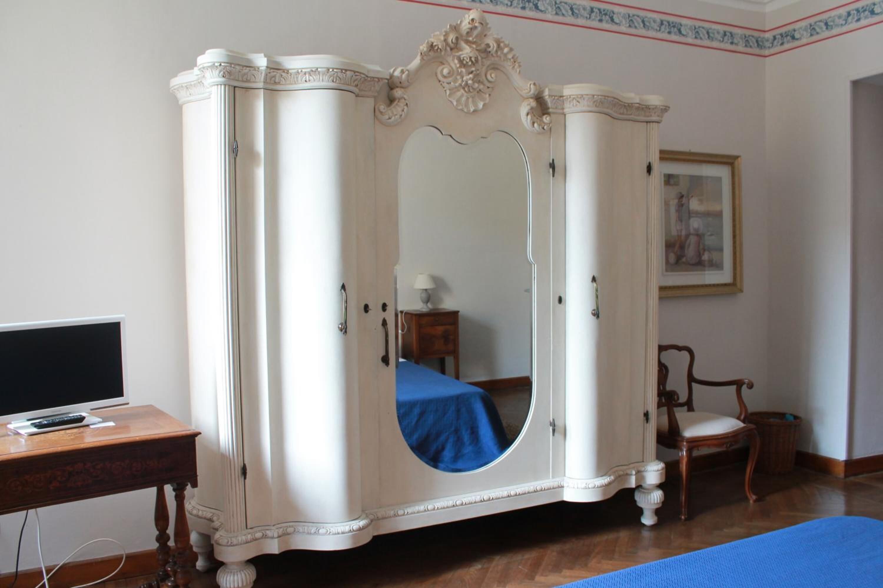 Una habitación con un armario blanco, un escritorio de madera con una computadora, una silla y una cama con colcha azul.