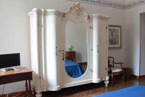 Una habitación con un armario blanco, un escritorio de madera con una computadora, una silla y una cama con colcha azul.