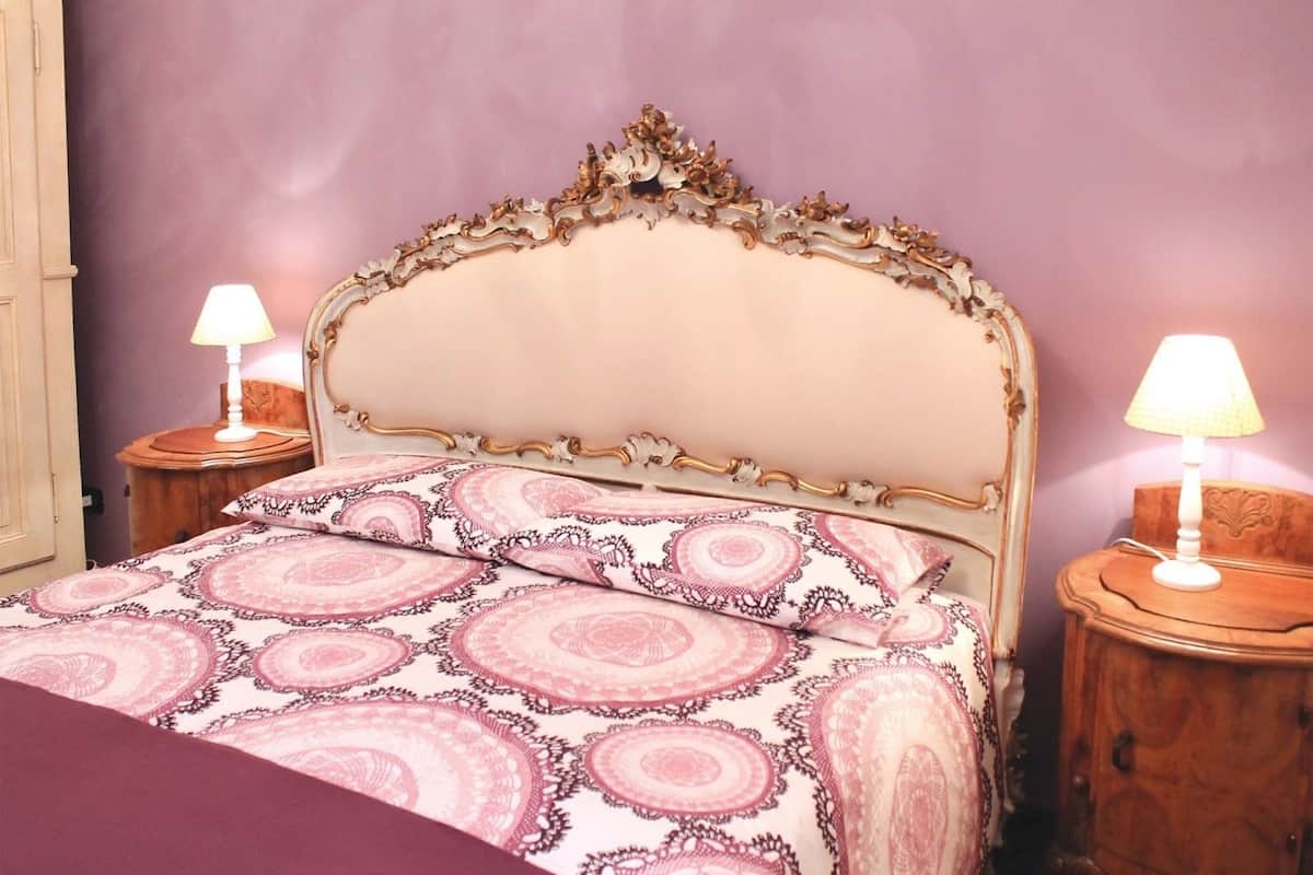 A bed with ornate headboard and matching nightstands, each with a lamp.
