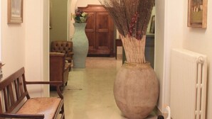 Un couloir avec un plafond en arc de cercle, un grand vase contenant des plantes séchées, un banc en bois, un radiateur et une petite figurine de canard.