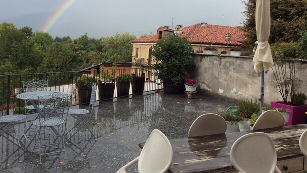 Une terrasse avec des sièges extérieurs, un arc-en-ciel en arrière-plan et une vue sur des bâtiments aux toits recouverts de tuiles rouges.