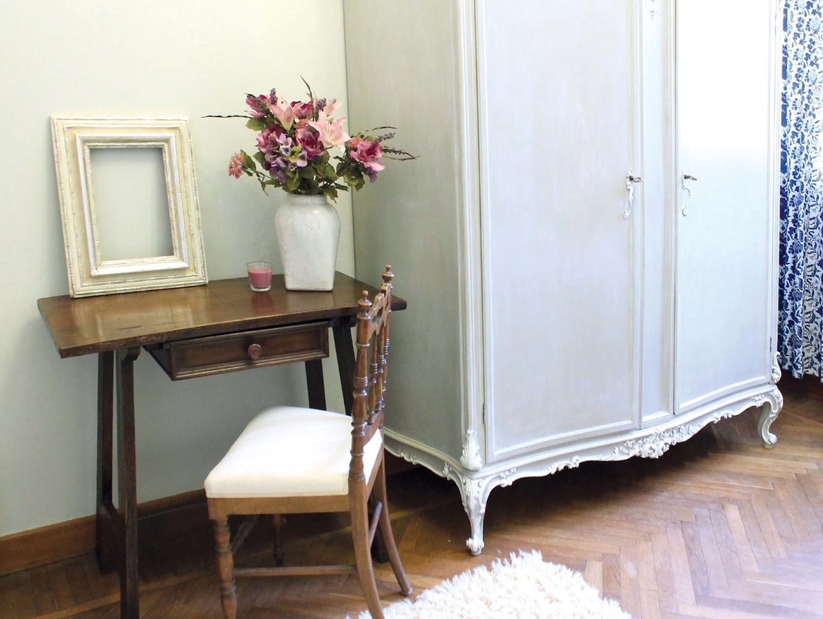 A room with a wooden desk, a chair, a white cabinet, and a vase with flowers.