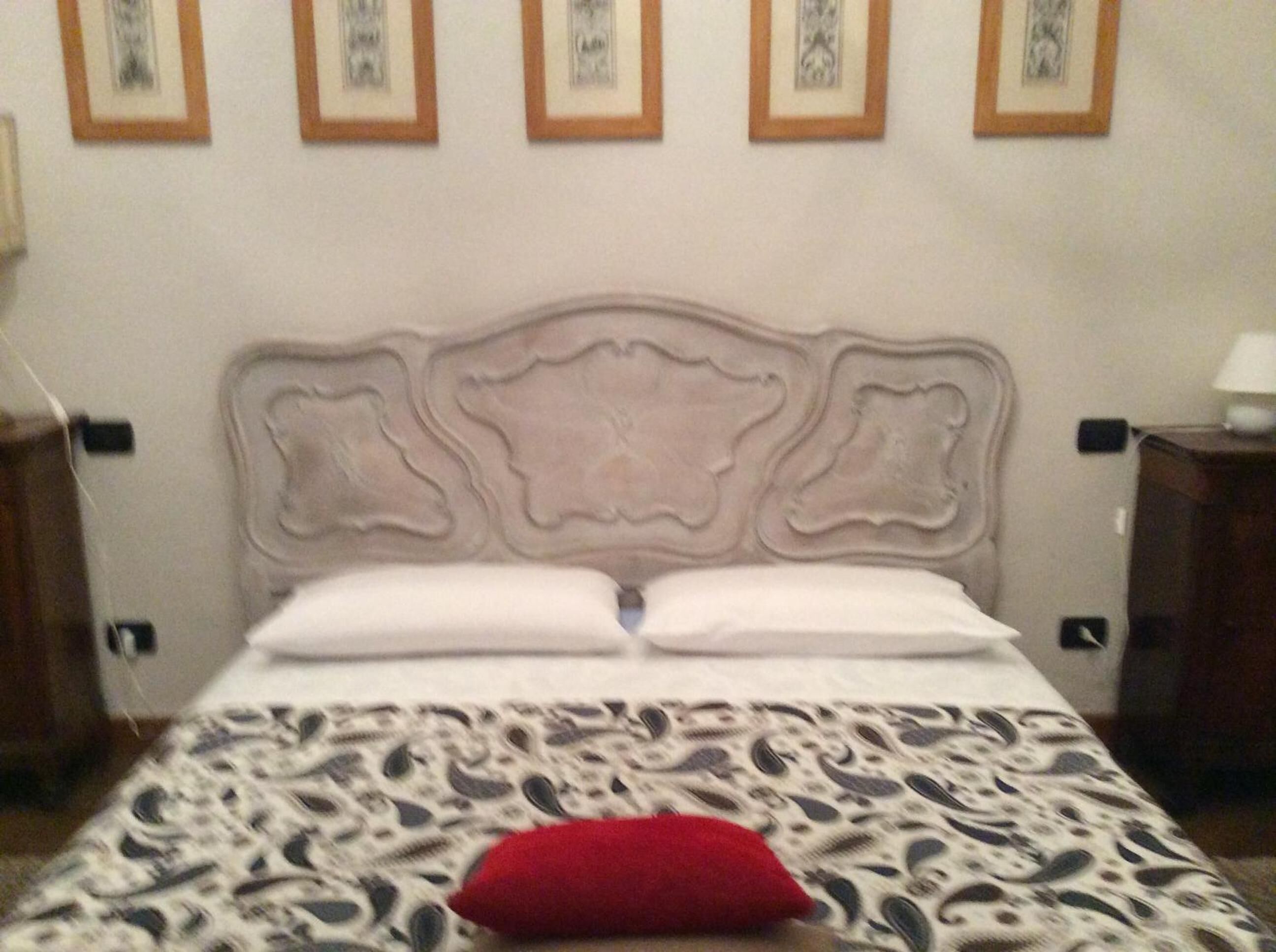 A bed with a patterned bedspread and a red pillow, framed by a decorative headboard.