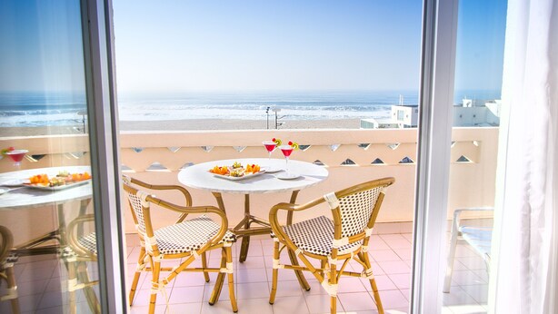 A balcony with a table and chairs overlooking the beach. -  THE ONE Grand Hotel da Póvoa 4 (Povoa De Varzim)