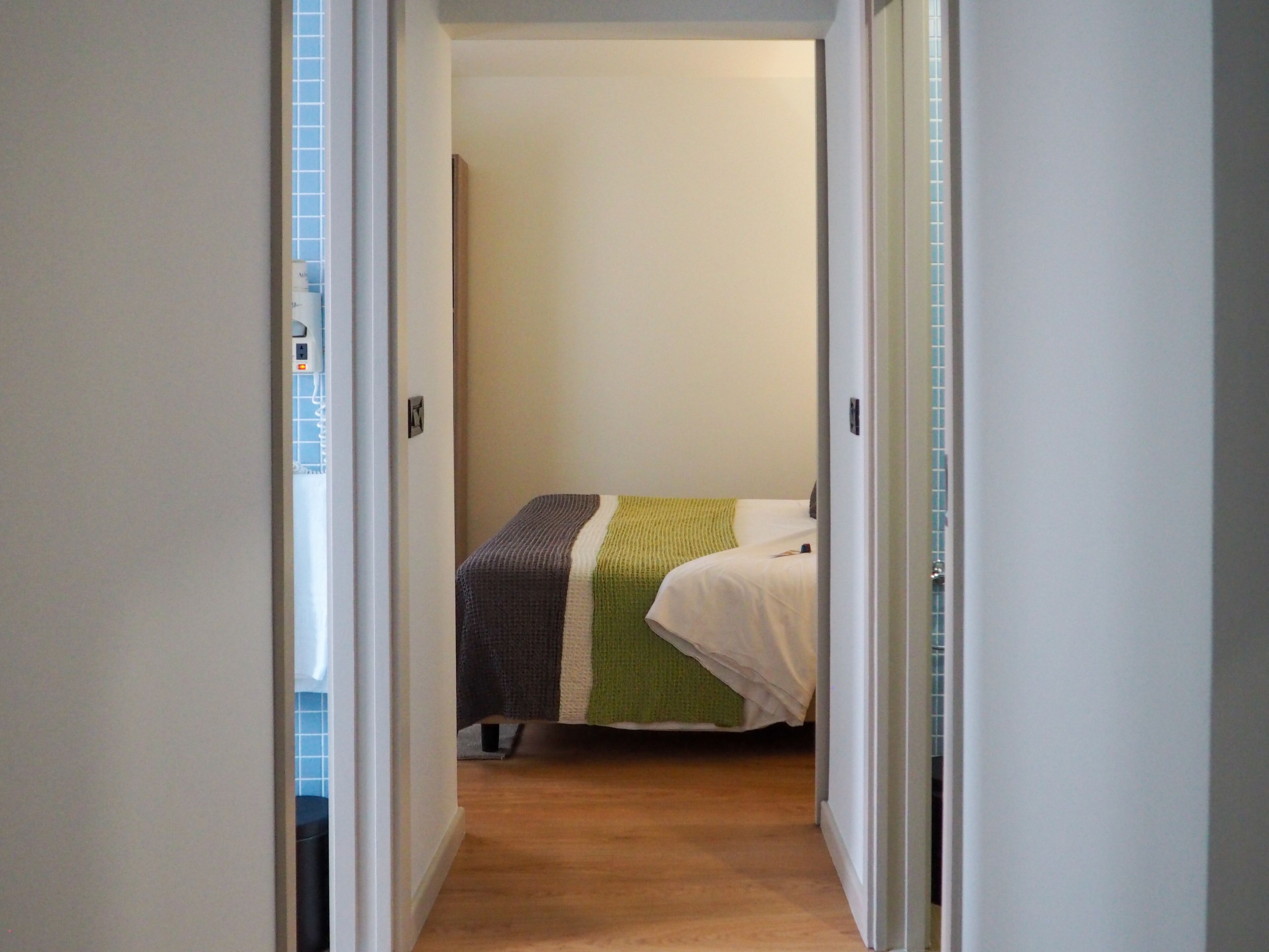 A narrow hallway leading to a bedroom with a bed covered in a striped blanket.