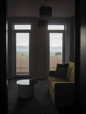 Une chambre d’hôtel avec un canapé, une table basse et une vue sur la plage, grâce à de grandes fenêtres.