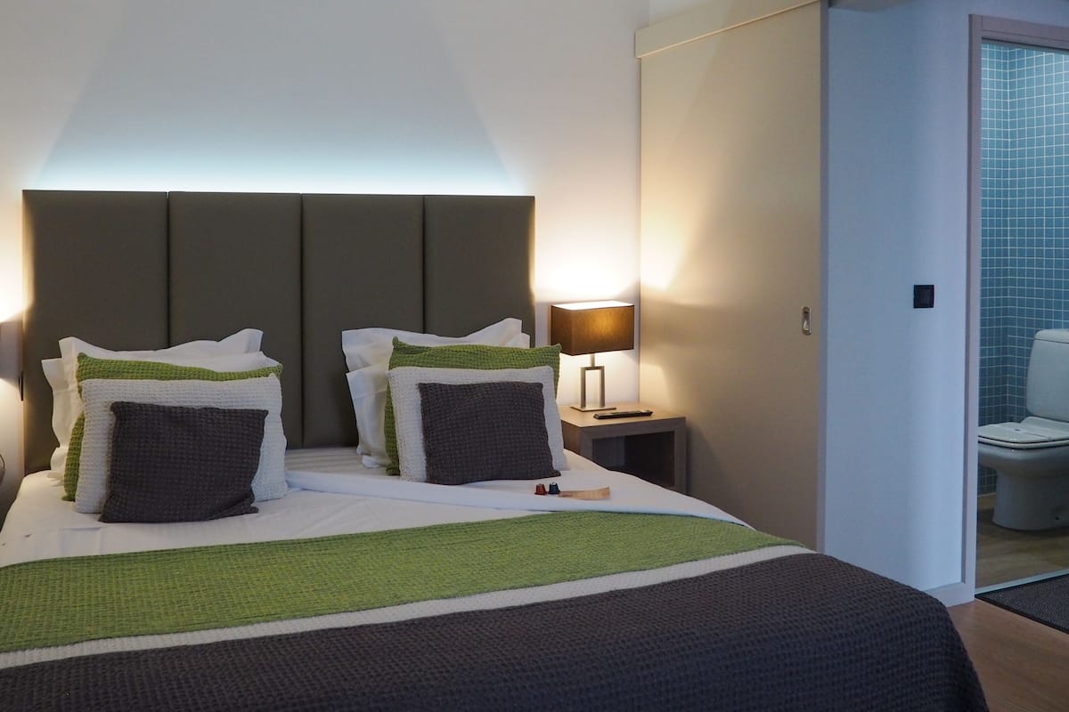 A hotel room with a bed, bedside lamp, and a view of the bathroom.