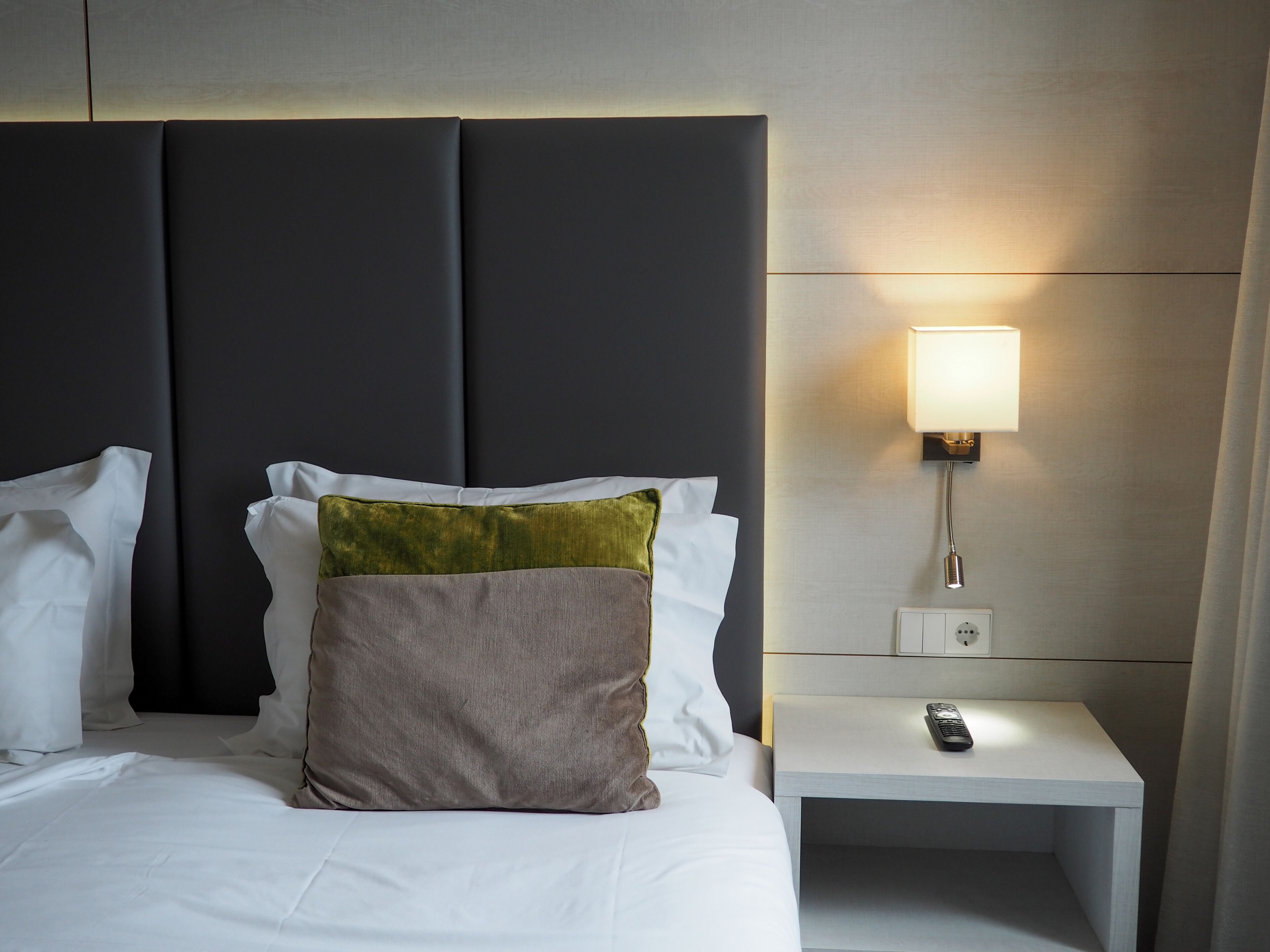 A hotel room with a large bed, a nightstand with a lamp, and a remote control.