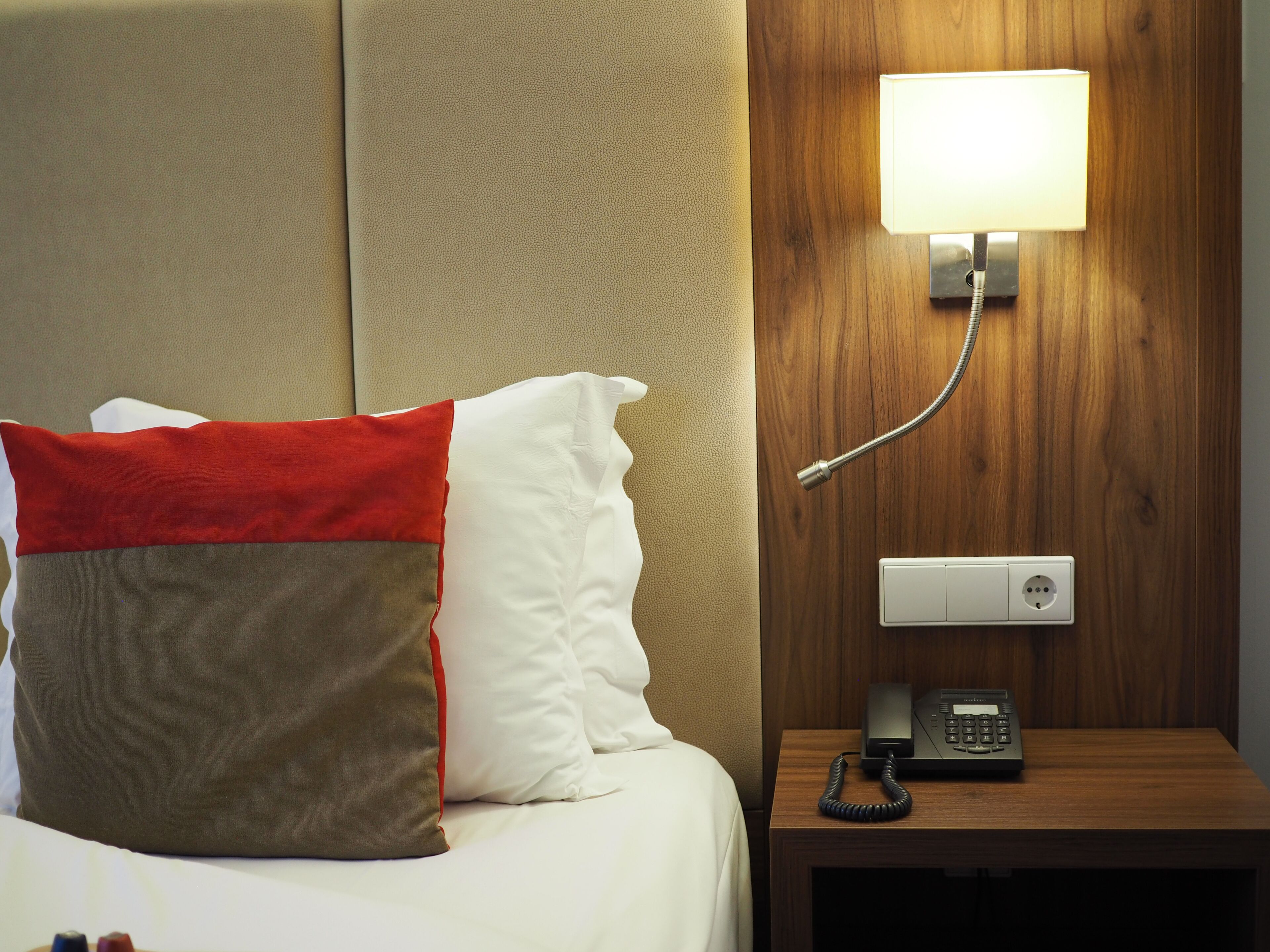 Una habitación de hotel con cama, almohadas, mesita de noche, lámpara y teléfono.