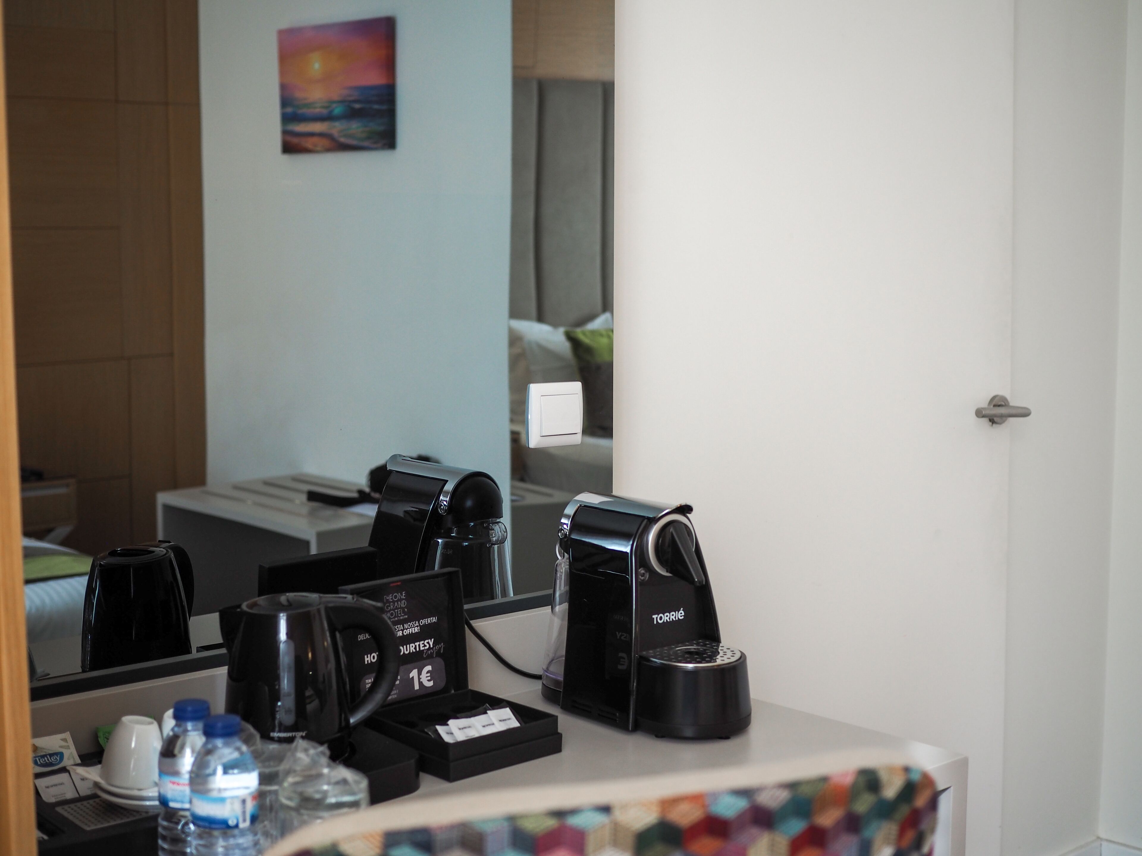 A hotel room with a coffee machine, a water bottle, and a small tray with a card and a coin.