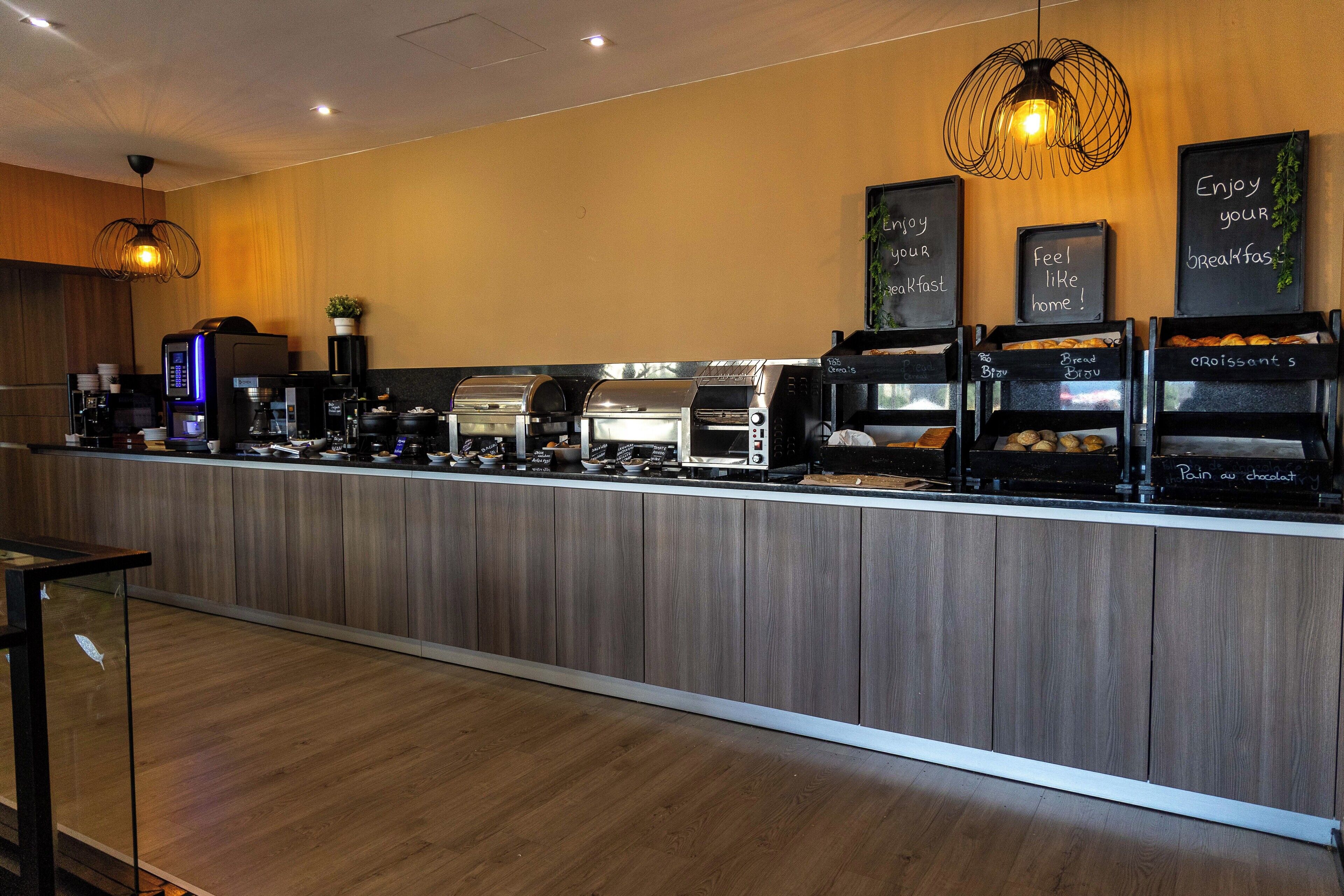 Un bar où l'on peut prendre le petit-déjeuner, avec des machines à café, une plante et des panneaux d'affichage en ardoise.