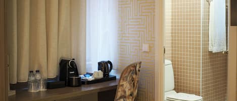 A bathroom with a toilet, a shower, and a sink. There is a chair with a patterned backrest and a towel hanging on the wall.