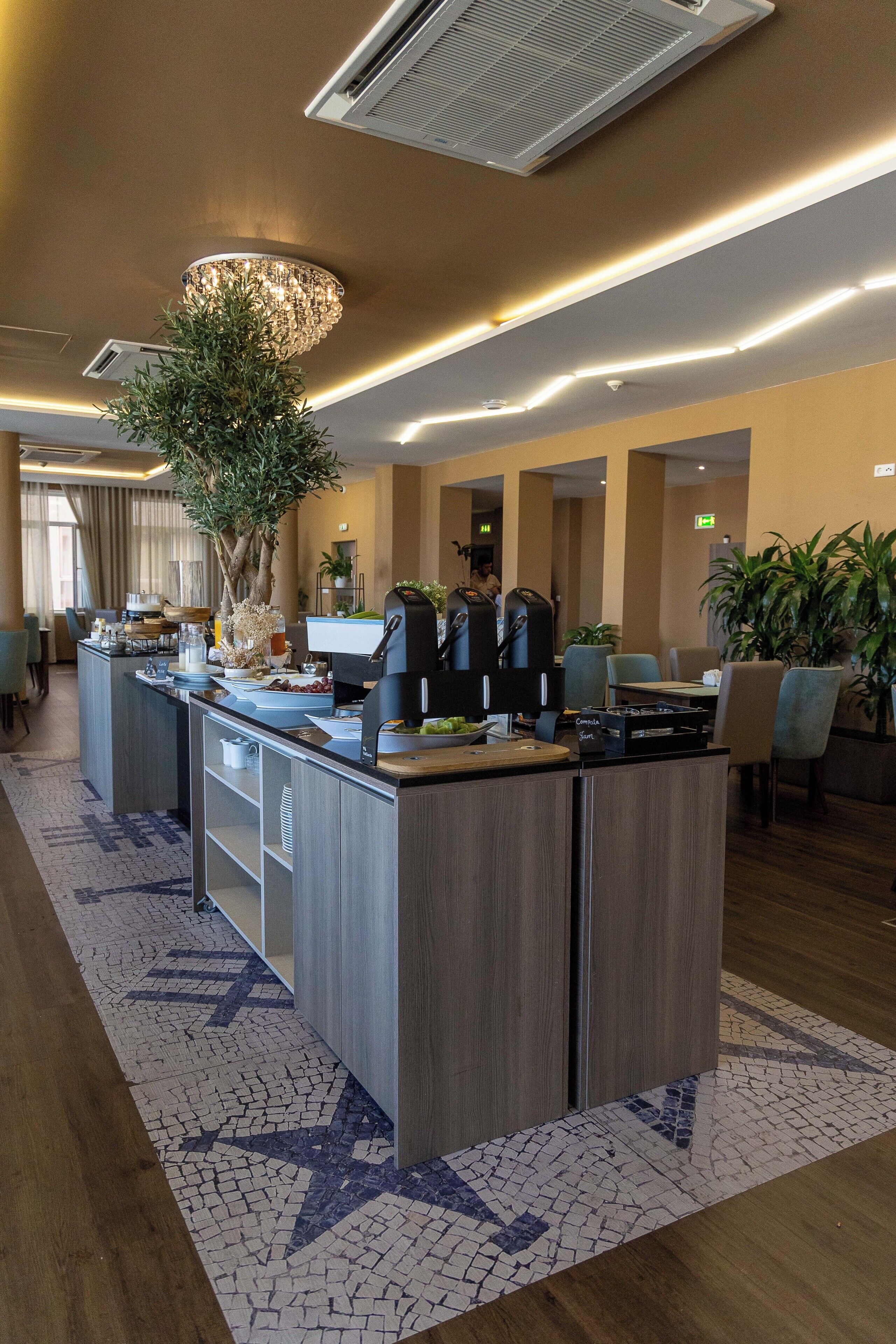 Un espace d’accueil d’hôtel avec un comptoir central, un grand lustre et une plante en pot.