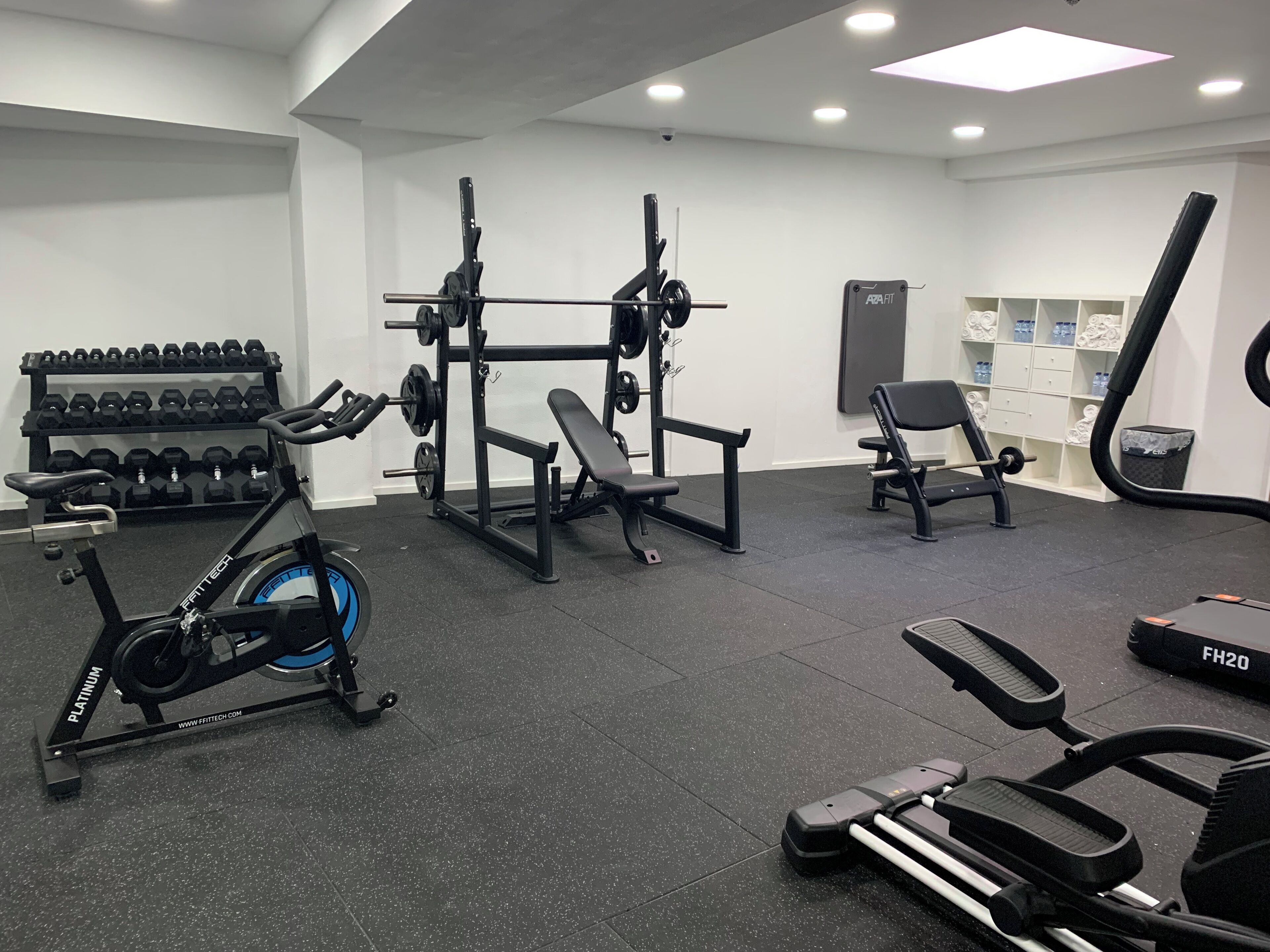 Uma academia com equipamentos de ginástica, incluindo bicicleta ergométrica, banco de musculação e halteres.