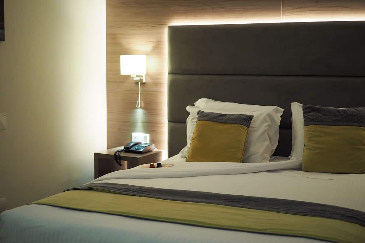 A neatly made bed with a headboard, a bedside table with a lamp, and a phone.