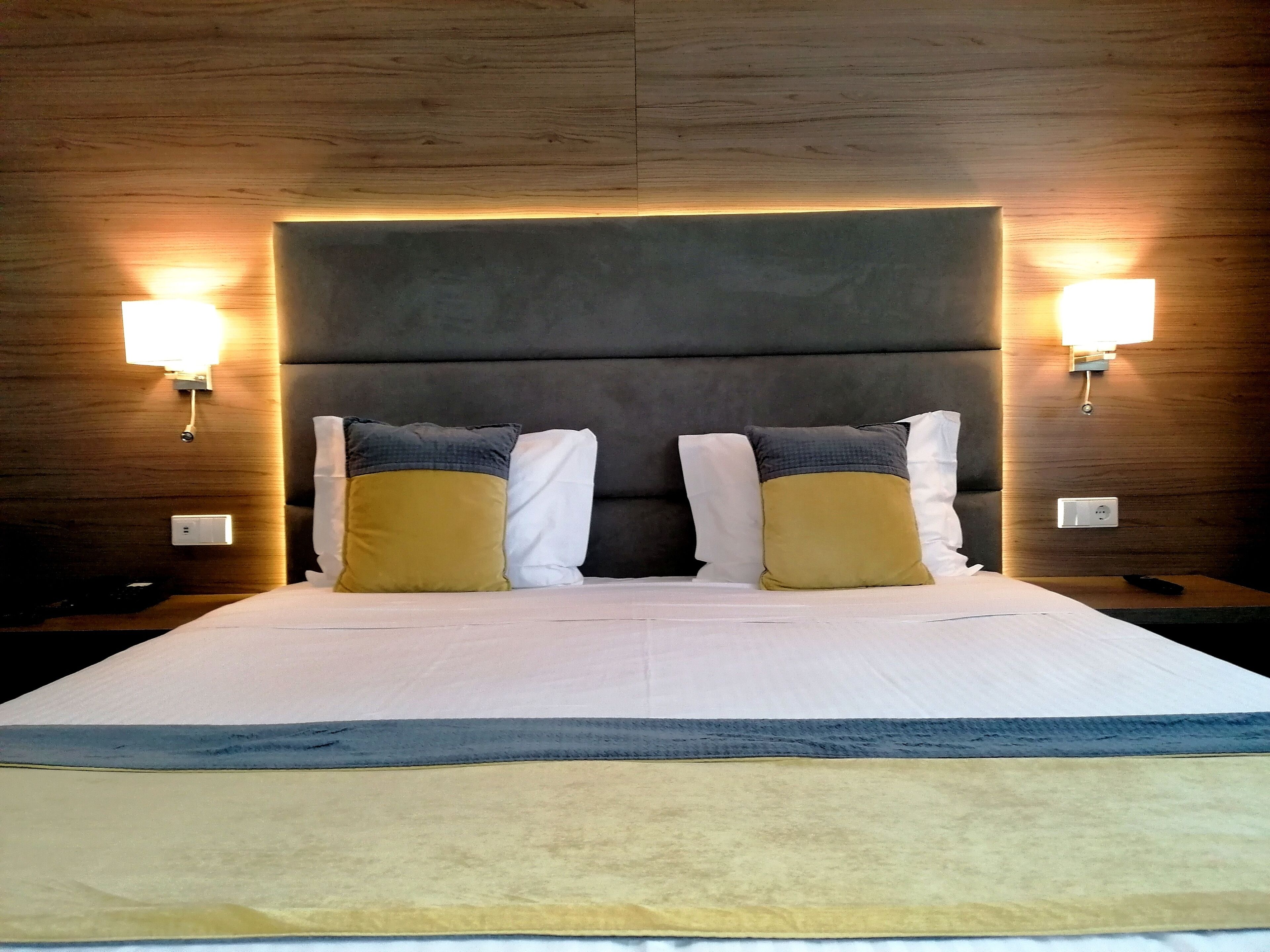 Ein Hotelzimmer mit einem großen Bett, zwei Nachttischlampen und einem hölzernen Kopfteil.