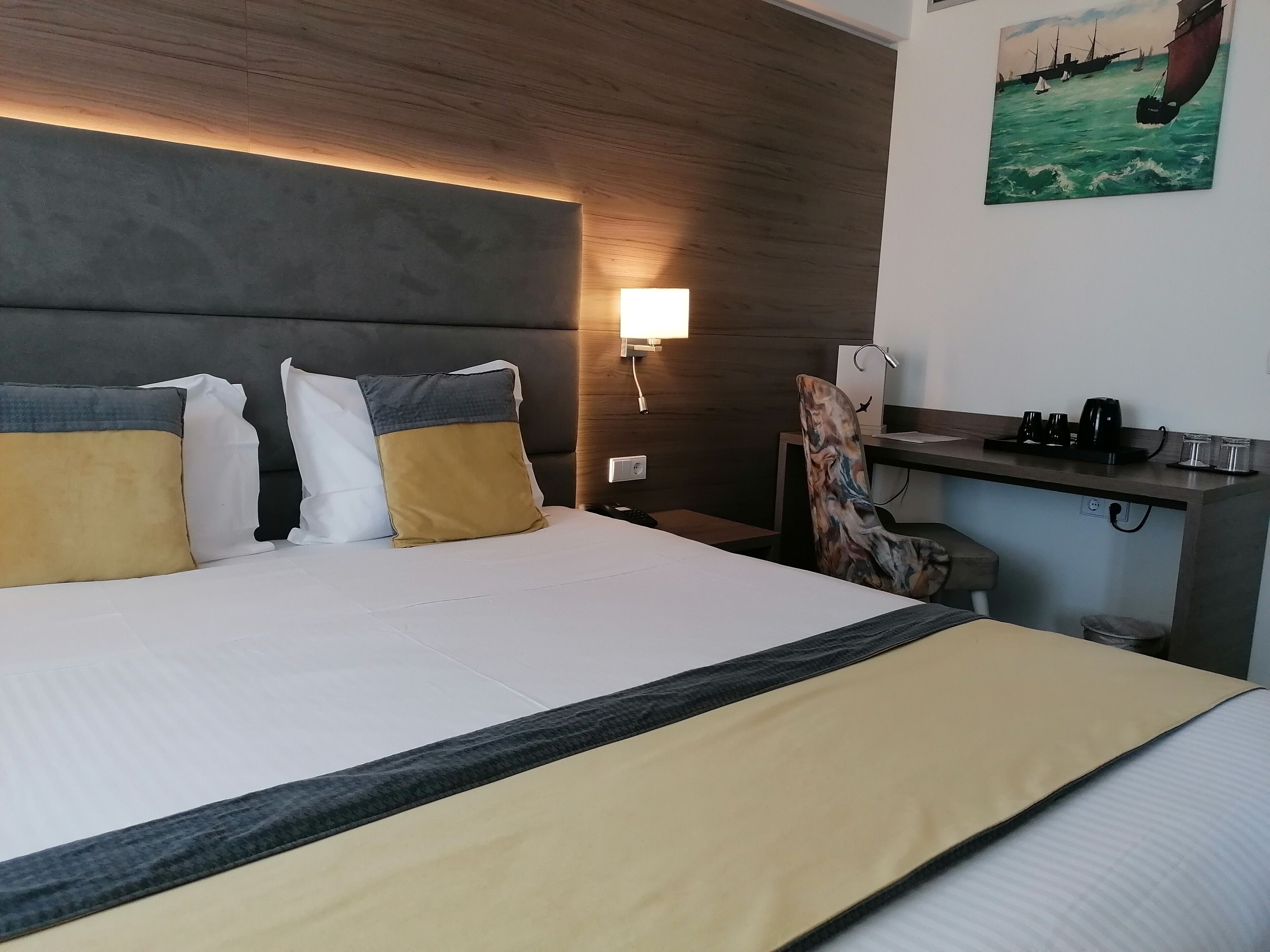 Una habitación de hotel con cama, escritorio y un cuadro de un velero en la pared.