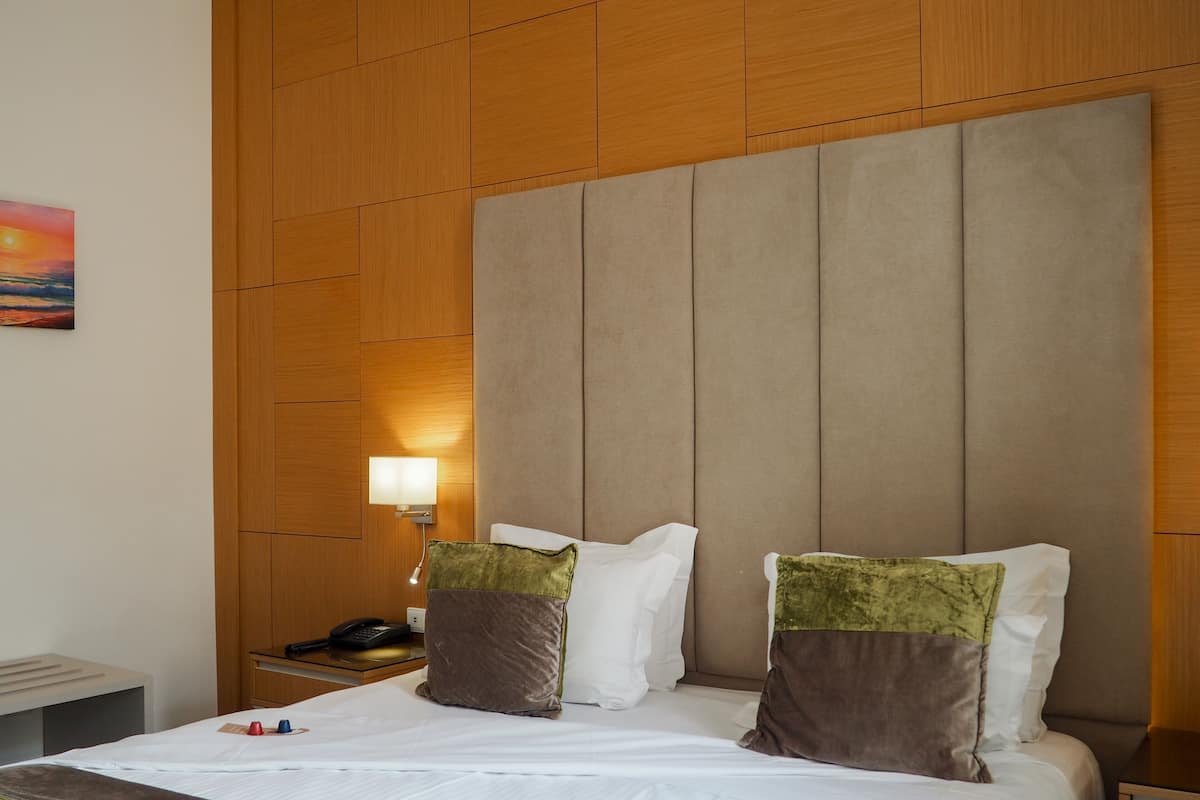A hotel room with a large bed, wooden panel walls, a nightstand with a phone, and a painting on the wall.