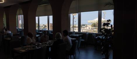Un comedor interior con mesas y sillas, ventanas amplias y vistas a la ciudad.