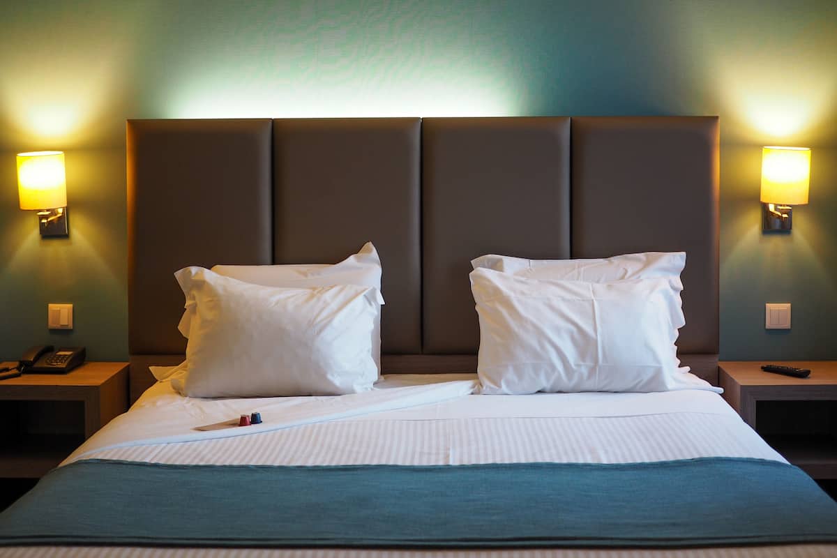 A hotel room with a large bed, two bedside lamps, a nightstand with a phone, and a remote control on the nightstand.