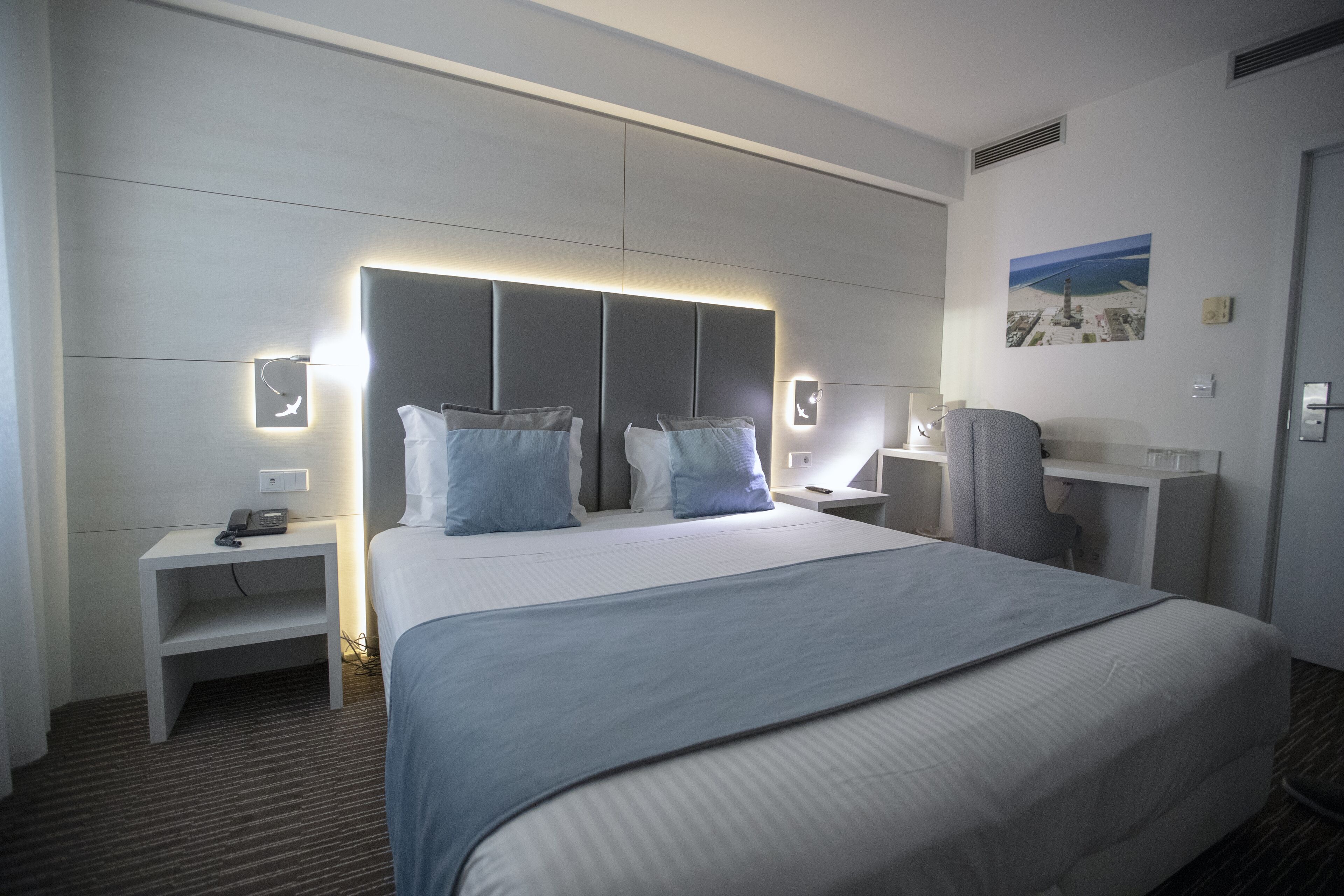 A modern hotel room with a large bed, bedside tables, a desk, and a chair.