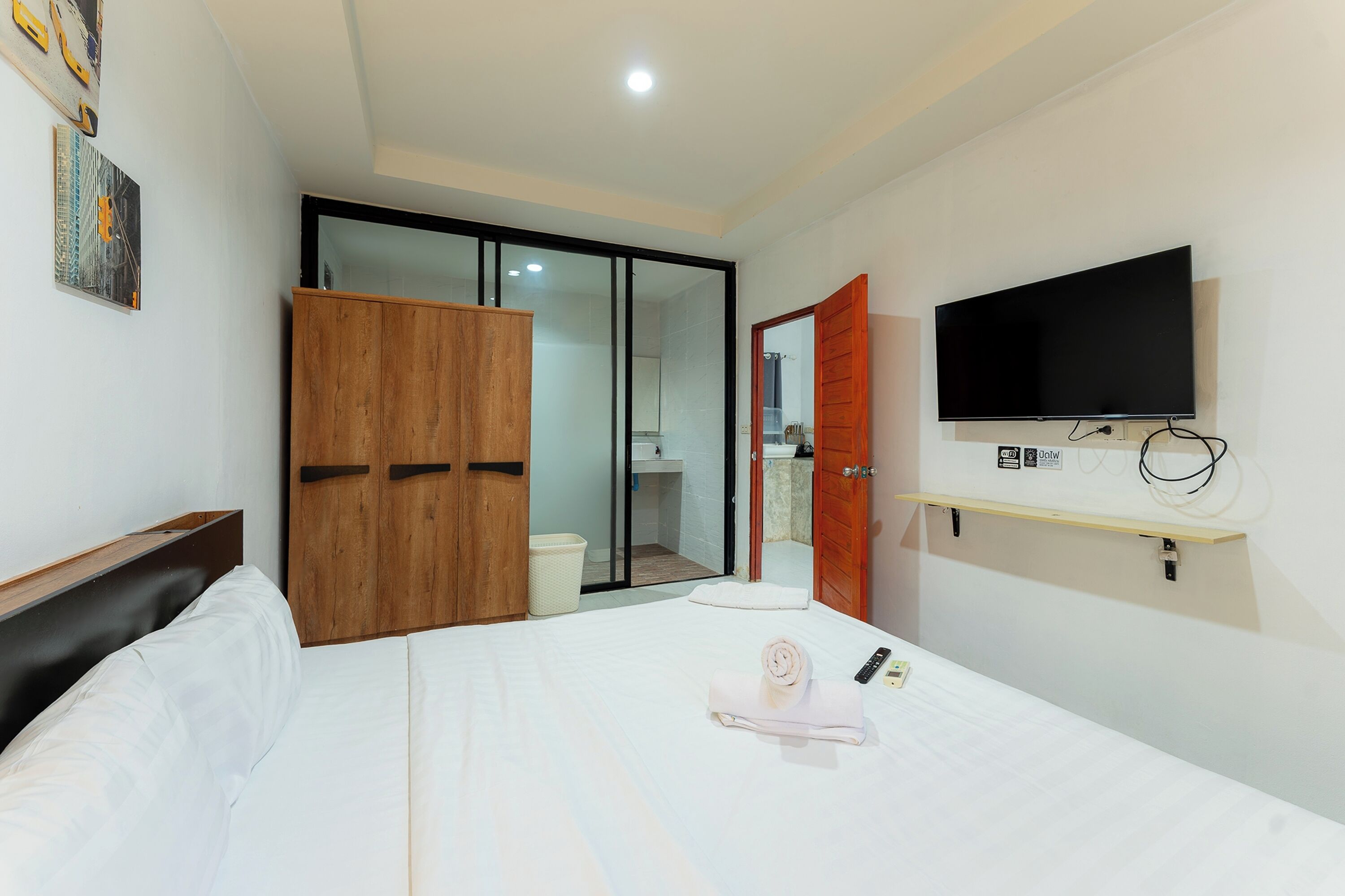 A hotel room with a bed, a wooden wardrobe, a television, and a bathroom visible through a glass door.