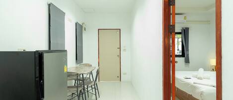 Habitación de hotel pequeña con cama, una mesa con sillas, un refrigerador y una puerta que da a otra habitación.