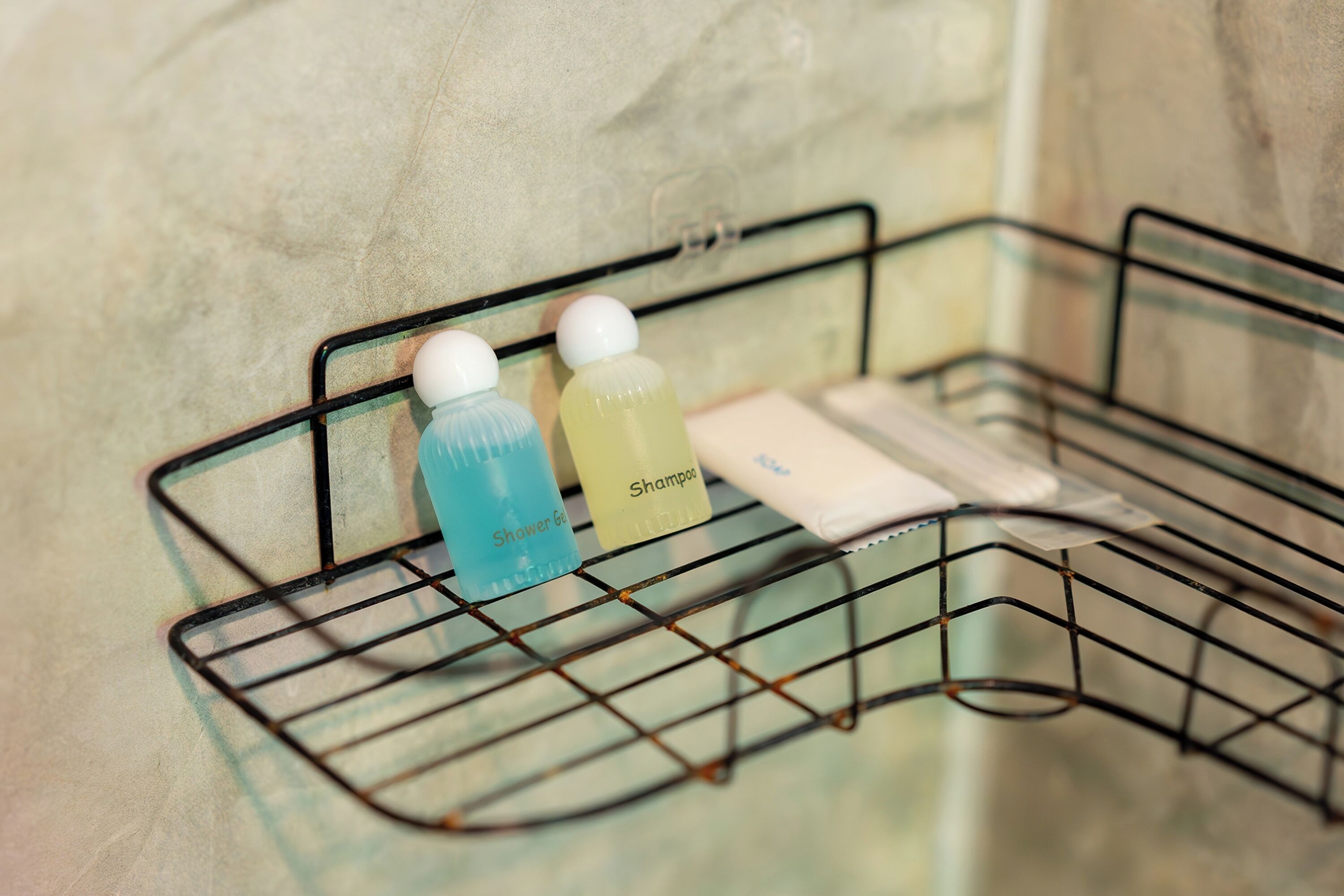 Une étagère en métal sur laquelle reposent deux bouteilles contenant un liquide et un objet blanc, vraisemblablement un mouchoir ou une serviette à main, le tout placé devant un mur texturé.