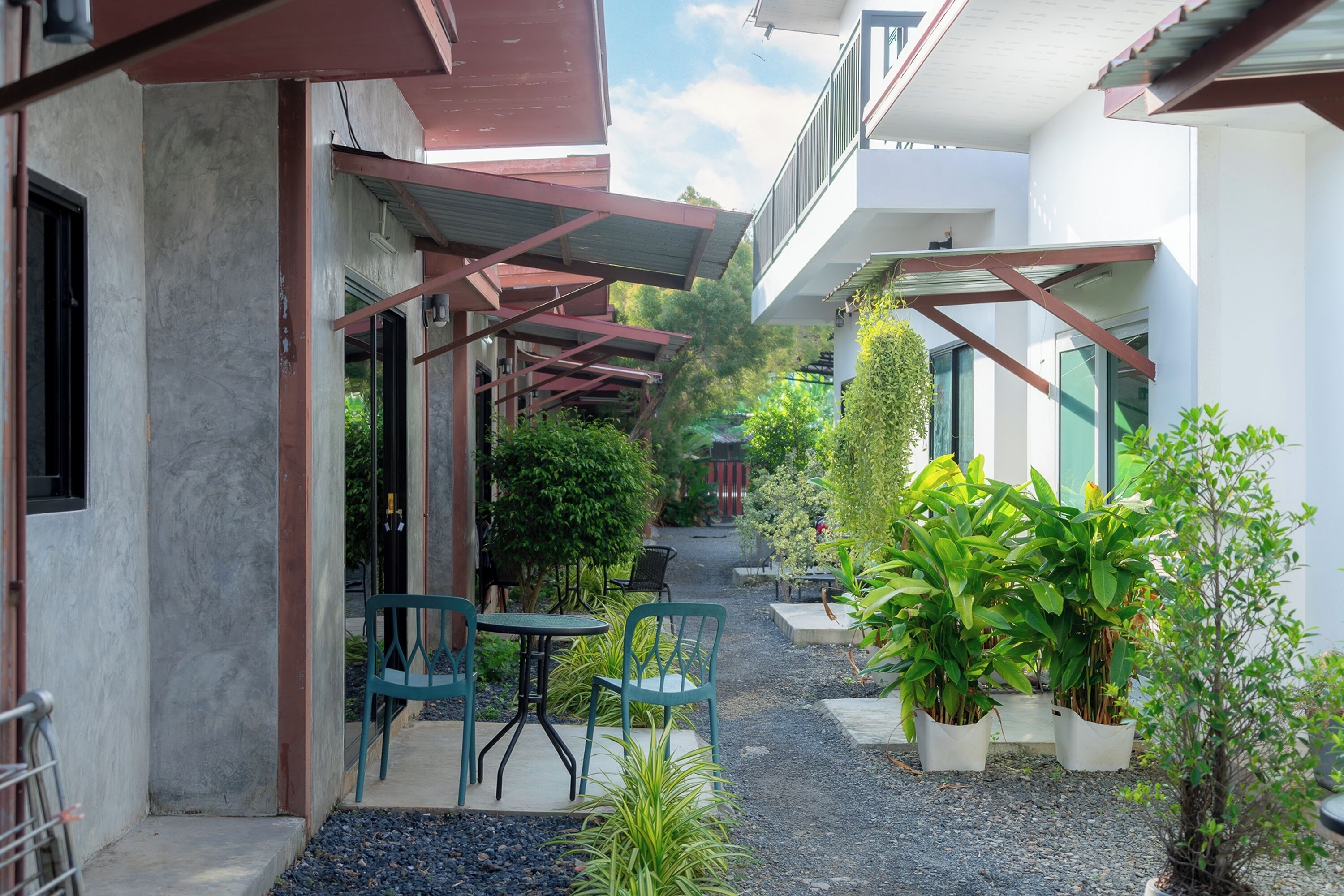 Une cour avec des espaces de repos en plein air, des plantes en pot et un chemin menant à l’entrée d’un bâtiment.