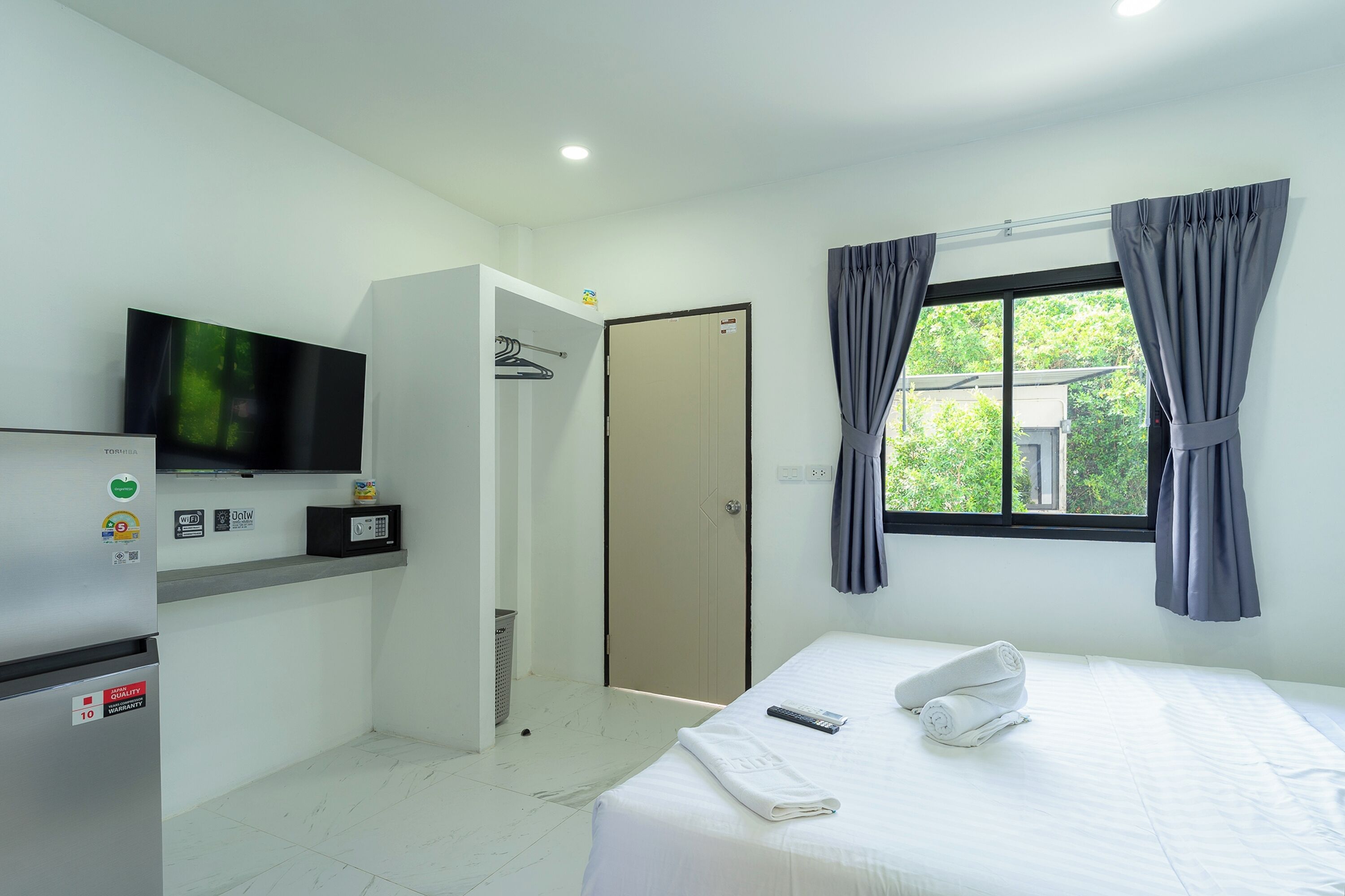 Une chambre d’hôtel équipée d’un lit, d’une télévision, d’un mini-réfrigérateur, d’une armoire et d’une fenêtre avec des rideaux.