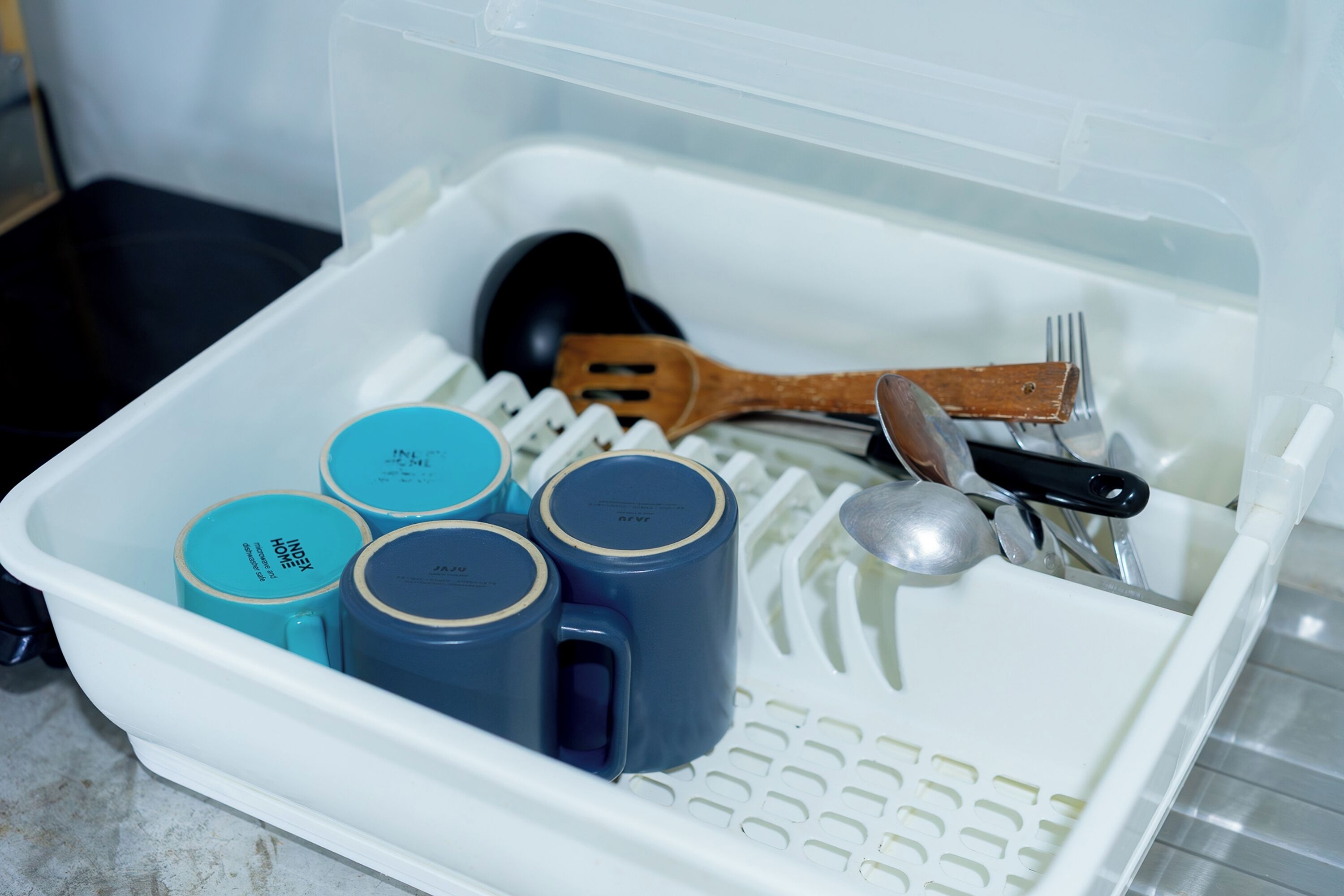 A kitchen drawer with utensils and blue mugs.