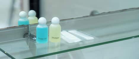 A bathroom with a glass shelf holding shampoo and shower gel bottles.