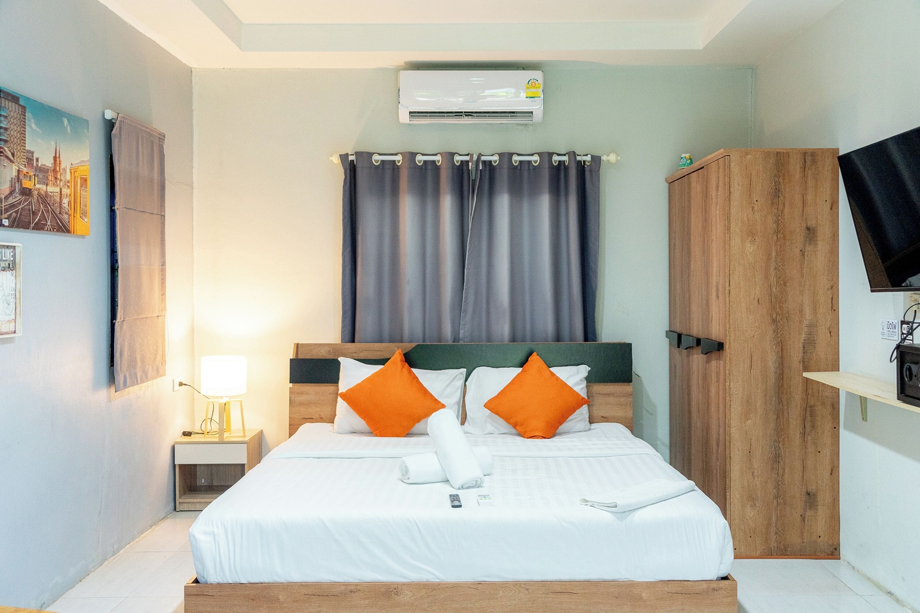 Habitación de hotel con una cama, aire acondicionado, mesita de noche con lámpara, armario de madera y televisión en la pared.