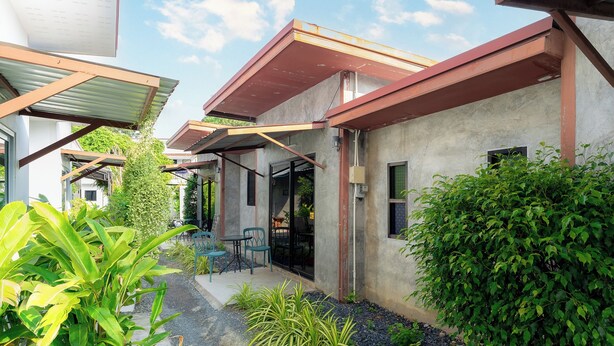A modern building with a covered patio area, outdoor seating, and lush greenery. - Malinee Resort (Choeng Thale)