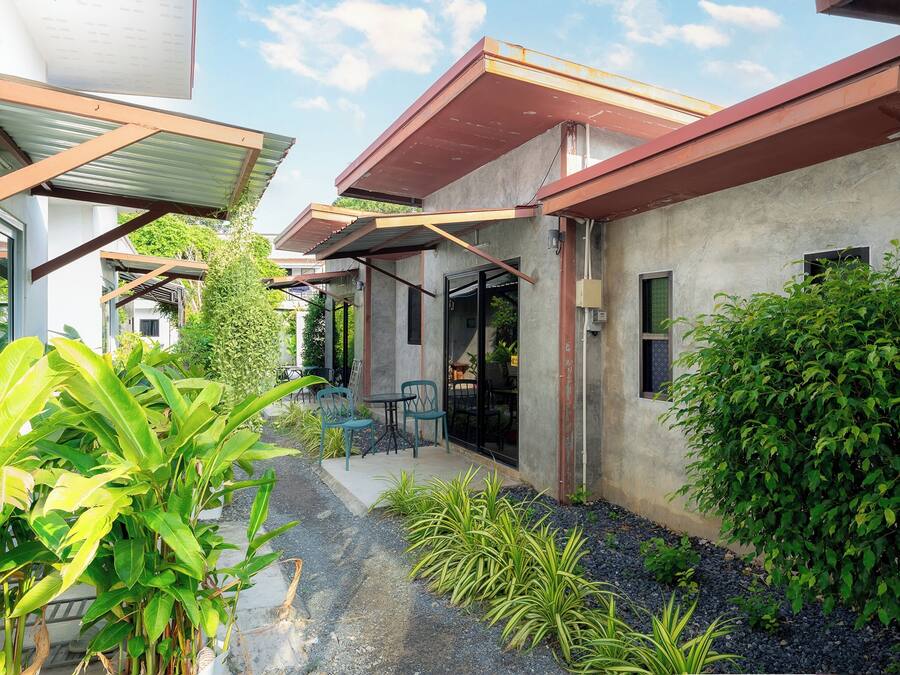 Un edificio moderno con un patio cubierto, mobiliario exterior y abundante vegetación.