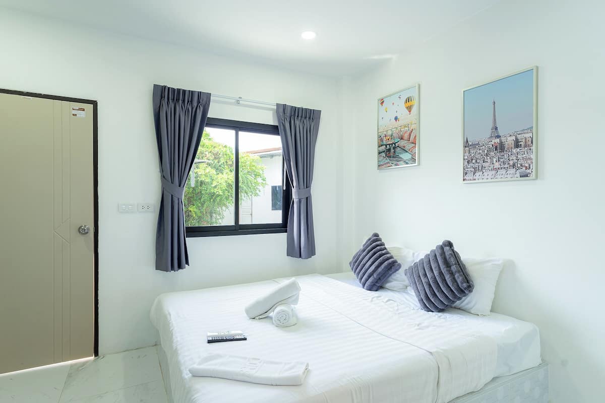 Een hotelkamer met een bed, een raam met gordijnen, een afstandsbediening, een handdoek en twee kunstwerken aan de muur.