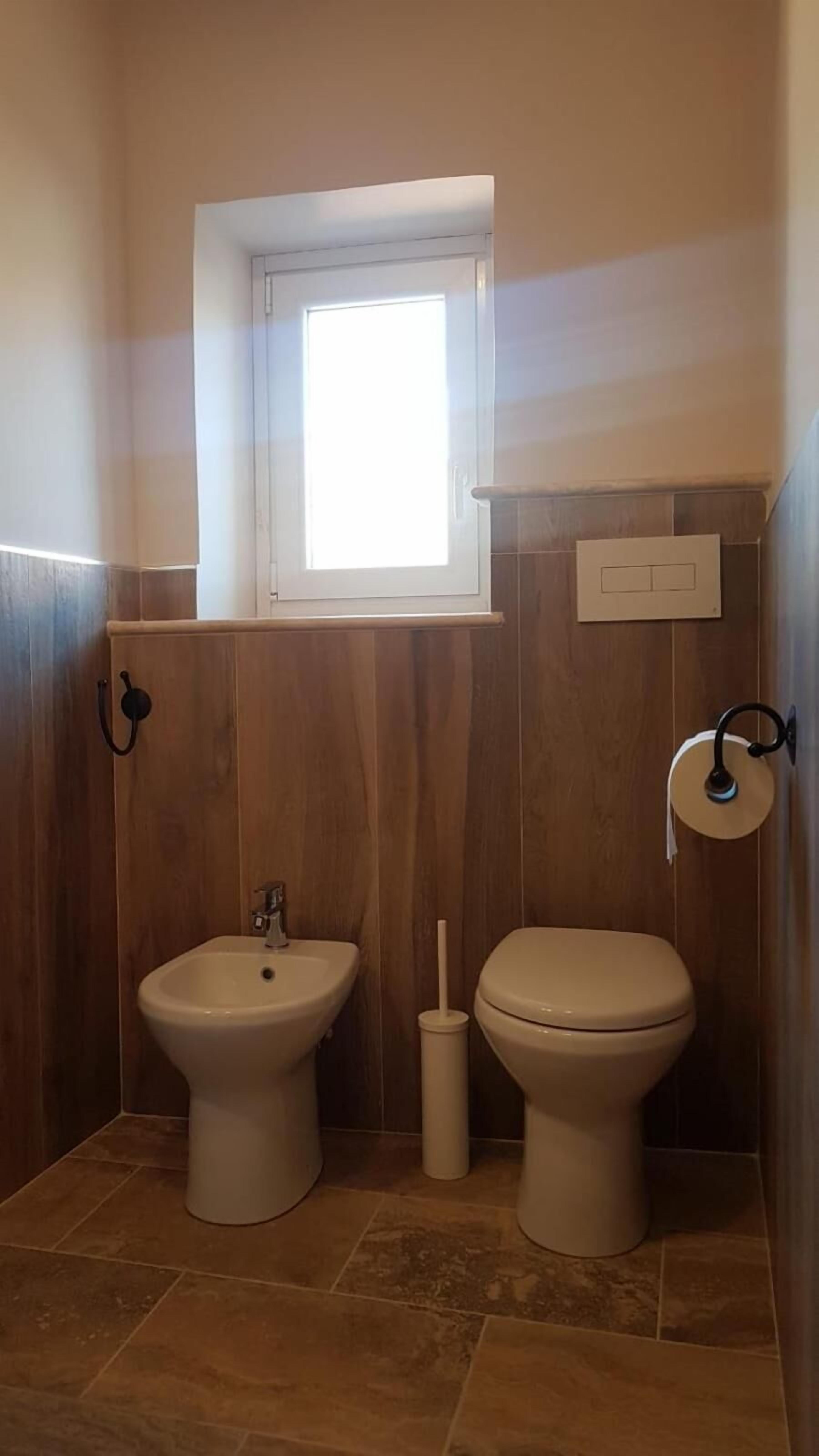 A bathroom with a bidet, toilet, and a window.