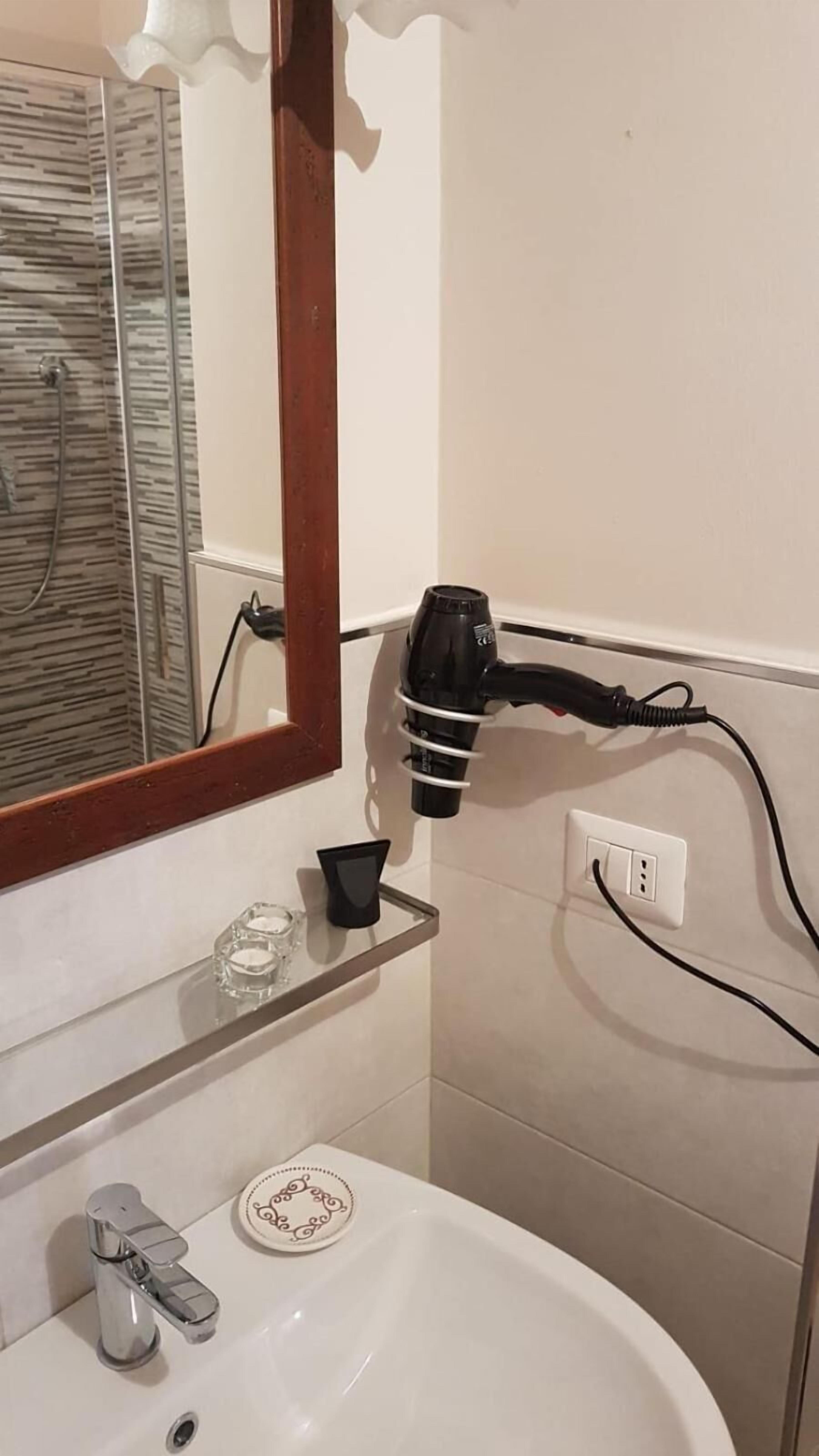 Een badkamer met een wastafel, spiegel en een haardroger aangesloten op een stopcontact.