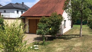 Une maison avec un toit recouvert de tuiles rouges, un petit jardin et un clocher.