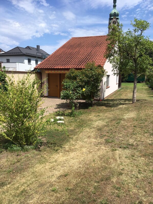 Una casa con techo de tejas rojas, un pequeño jardín y una torre del reloj.