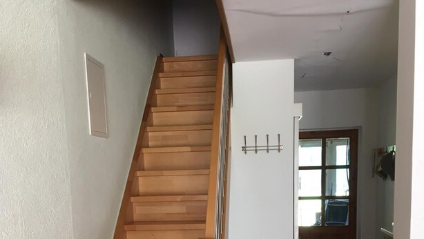 Un escalier en bois menant à un palier avec un mur blanc et une porte dotée d’une fenêtre.