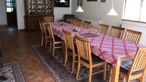 Un espace repas avec une longue table recouverte d’une nappe à motifs, entourée de chaises en bois.