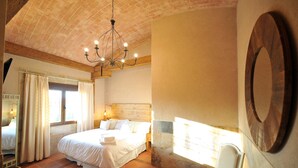 A bedroom with a large bed, a chandelier, a window with curtains, and a chair. - Rural house 5 * Grand Luxury in Toledo, Puy Du Fou (Albarreal de Tajo)