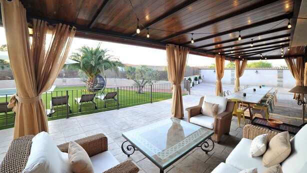 An outdoor patio with wooden ceiling, cushioned seating, and a glass table. - Rural house 5 * Grand Luxury in Toledo, Puy Du Fou (Albarreal de Tajo)