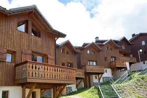 Filas de edificios de estilo chalete de madera con balcones, una pared de piedra y una escalera que sube.