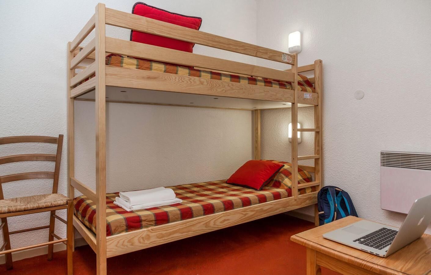 Een slaapkamer met een stapelbed, een bureau en stoel, een laptop en een verwarming.